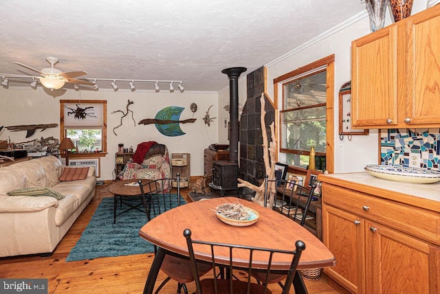 living room featuring a textured ceiling, ceiling fan, crown molding, light hardwood / wood-style flooring, and a wood stove