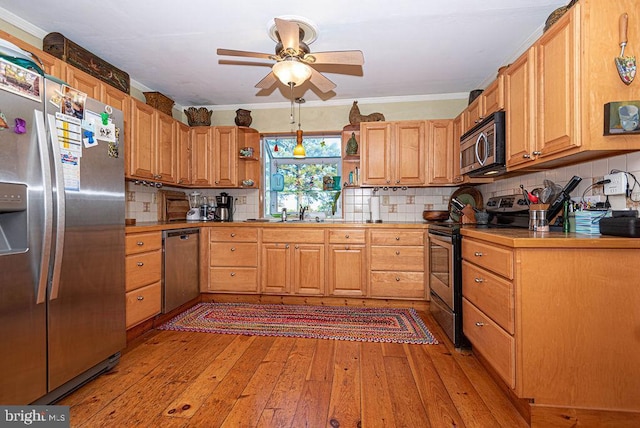 kitchen featuring light wood-type flooring, tasteful backsplash, stainless steel appliances, ceiling fan, and crown molding