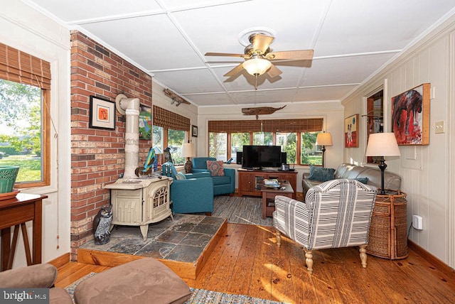 living room with a wood stove, ceiling fan, wood-type flooring, and brick wall