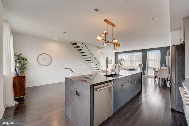 kitchen featuring dark hardwood / wood-style flooring, a center island with sink, an inviting chandelier, and appliances with stainless steel finishes