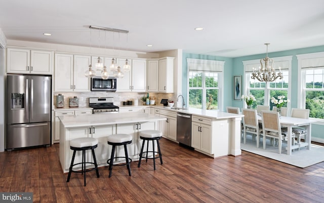 kitchen featuring appliances with stainless steel finishes, backsplash, a kitchen island, white cabinetry, and hanging light fixtures