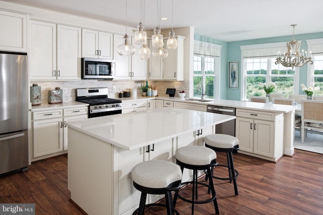 kitchen with appliances with stainless steel finishes, tasteful backsplash, sink, decorative light fixtures, and a center island