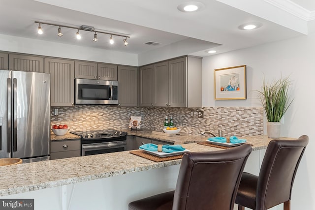 kitchen featuring a breakfast bar area, backsplash, light stone counters, and stainless steel appliances