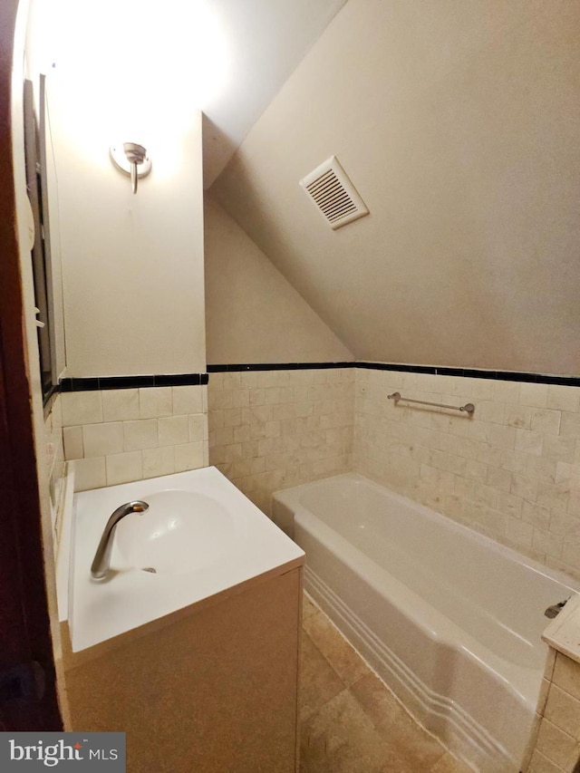 bathroom with vaulted ceiling, tile walls, tile patterned flooring, vanity, and a washtub