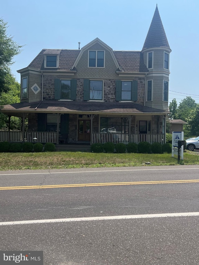 view of front of house with covered porch, stone siding, and roof with shingles