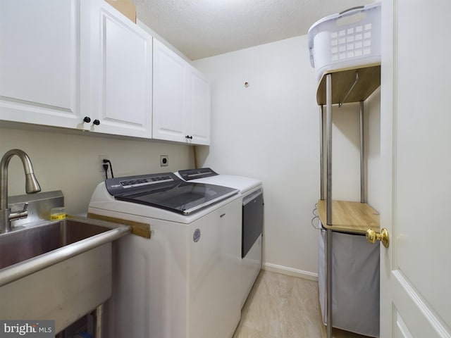 washroom with cabinets, a textured ceiling, washing machine and dryer, and sink