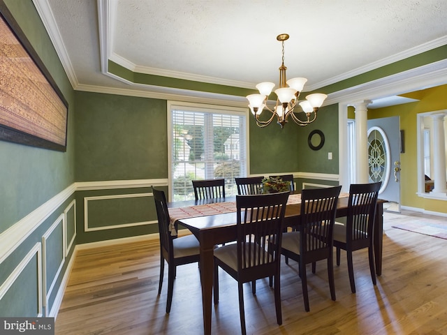 dining space with ornate columns, a tray ceiling, crown molding, hardwood / wood-style flooring, and a notable chandelier