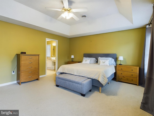 bedroom with light carpet, ensuite bath, a raised ceiling, and ceiling fan