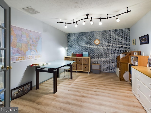 home office featuring light hardwood / wood-style flooring, brick wall, and a textured ceiling