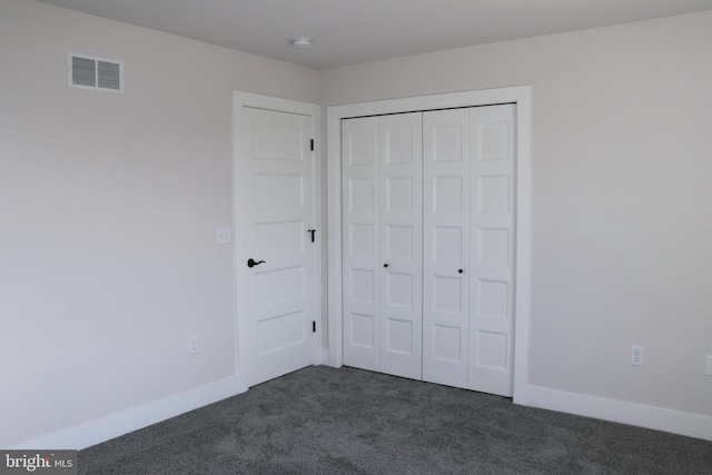 unfurnished bedroom with dark colored carpet and a closet