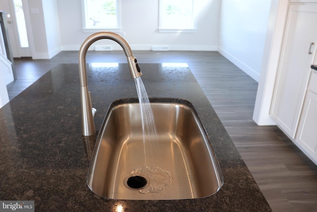 details with white cabinetry, sink, dark stone countertops, and dark wood-type flooring