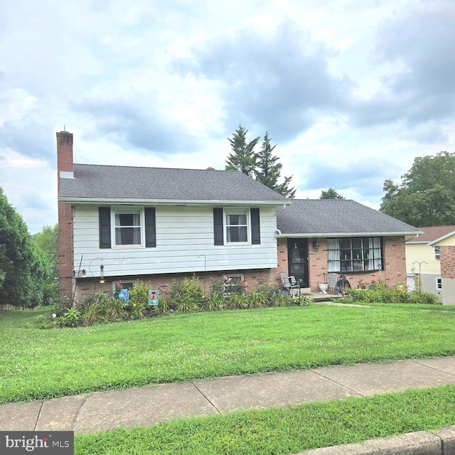 split level home with a front lawn, a chimney, a shingled roof, and brick siding