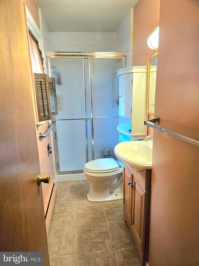 bathroom with toilet, a baseboard heating unit, vanity, a shower stall, and stone finish flooring