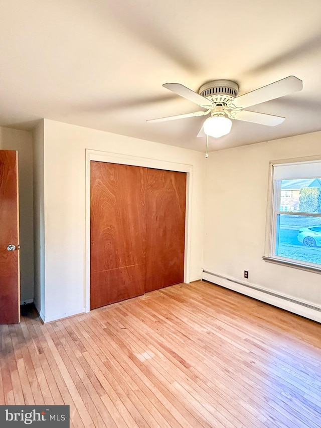 unfurnished bedroom with hardwood / wood-style floors, baseboard heating, a closet, and a ceiling fan