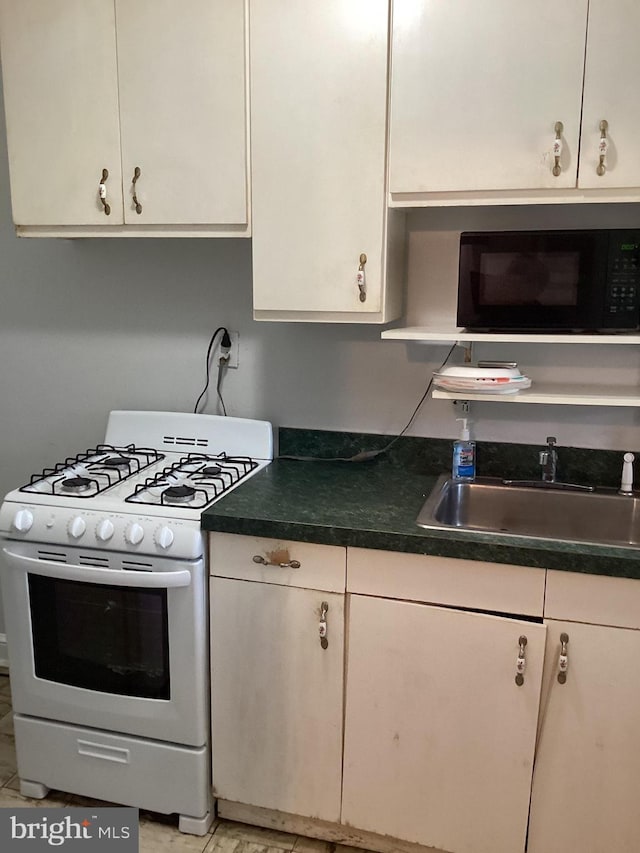 kitchen featuring white cabinets, white gas stove, light tile patterned floors, and sink