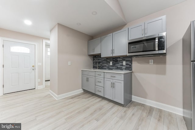 kitchen with stainless steel appliances, gray cabinetry, backsplash, light hardwood / wood-style flooring, and sink