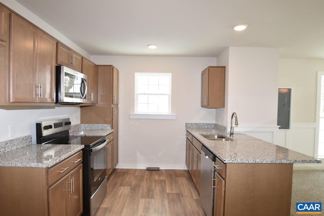 kitchen featuring sink, appliances with stainless steel finishes, electric panel, light stone counters, and kitchen peninsula