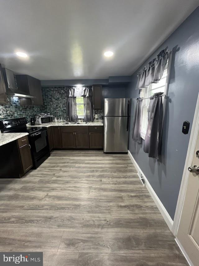 kitchen with stainless steel refrigerator, electric range, tasteful backsplash, dark brown cabinets, and light wood-type flooring