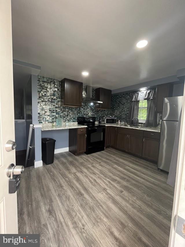 kitchen featuring tasteful backsplash, dark brown cabinets, stainless steel appliances, wall chimney range hood, and hardwood / wood-style floors