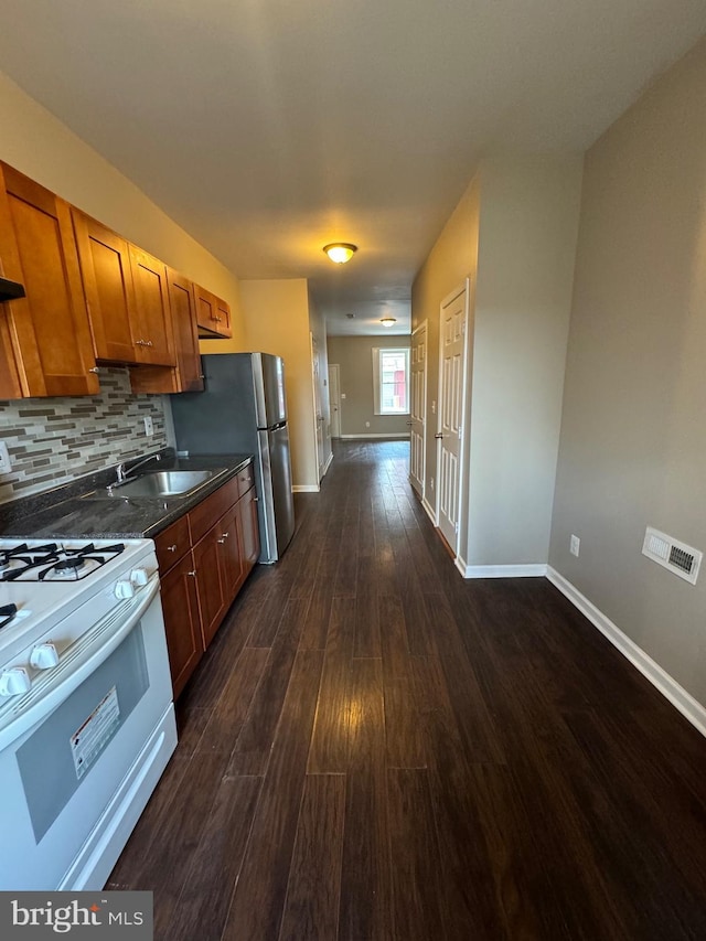 kitchen with white range with gas stovetop, backsplash, dark wood-type flooring, stainless steel refrigerator, and sink