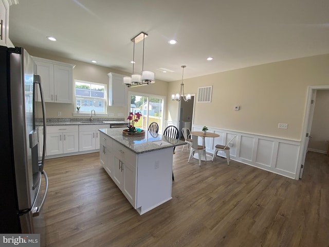 kitchen with a kitchen island, sink, decorative light fixtures, white cabinets, and stainless steel refrigerator