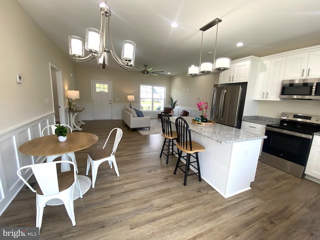 kitchen with white cabinetry, stainless steel appliances, pendant lighting, a kitchen island, and ceiling fan with notable chandelier