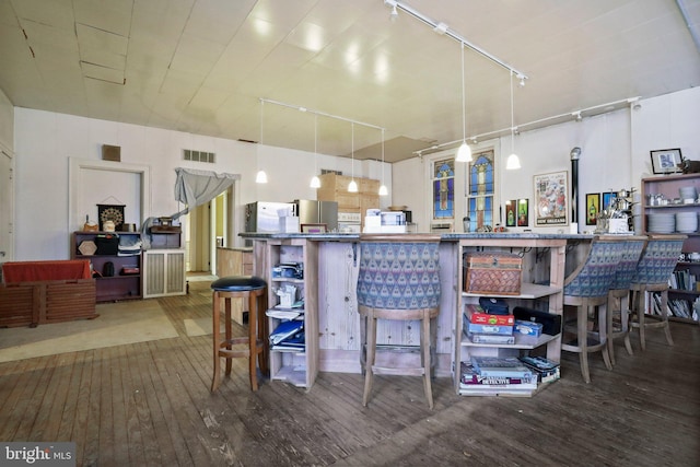 kitchen featuring a kitchen bar, stainless steel fridge, rail lighting, dark hardwood / wood-style floors, and hanging light fixtures