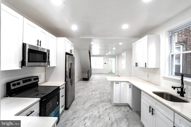 kitchen with kitchen peninsula, appliances with stainless steel finishes, white cabinetry, and sink