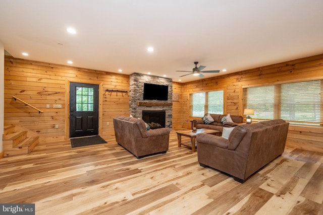 living room featuring a stone fireplace, ceiling fan, light hardwood / wood-style flooring, and wood walls