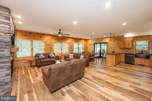 living room with ceiling fan, sink, a stone fireplace, light hardwood / wood-style flooring, and wood walls