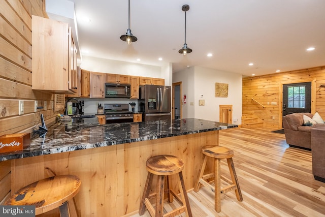 kitchen featuring sink, a kitchen breakfast bar, pendant lighting, wooden walls, and appliances with stainless steel finishes