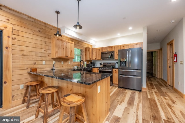 kitchen with kitchen peninsula, wooden walls, black appliances, pendant lighting, and dark stone countertops