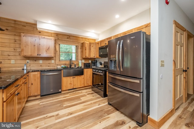 kitchen with black appliances, sink, dark stone counters, and light hardwood / wood-style flooring