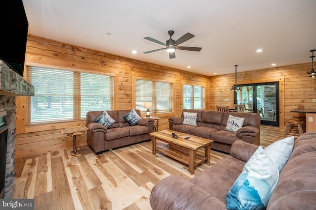 living room featuring a stone fireplace, ceiling fan, wood walls, and light wood-type flooring