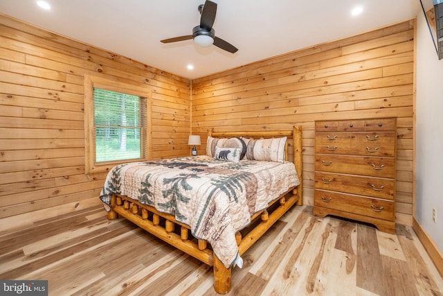 bedroom with ceiling fan, wooden walls, and light hardwood / wood-style flooring