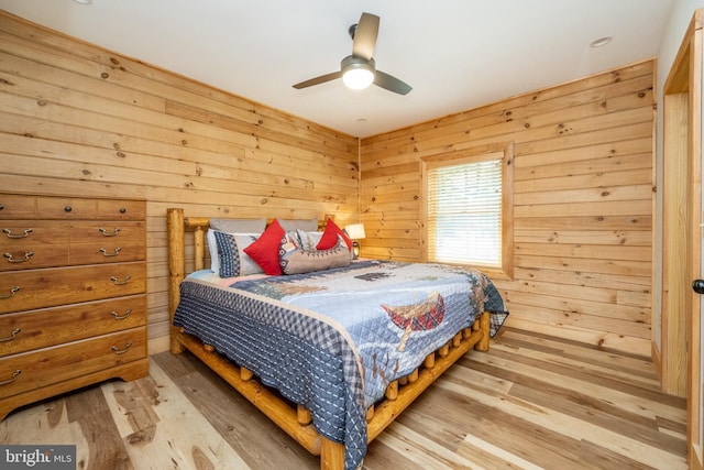 bedroom with light hardwood / wood-style floors, ceiling fan, and wooden walls