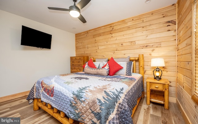 bedroom with hardwood / wood-style flooring, ceiling fan, and wood walls