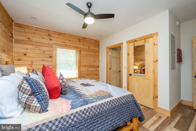 bedroom with electric panel, light hardwood / wood-style floors, ceiling fan, and wooden walls