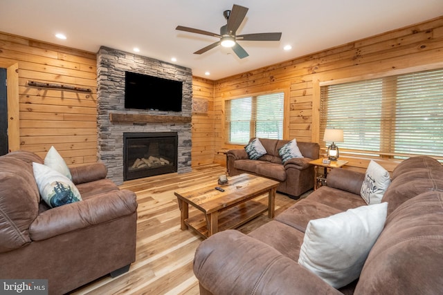 living room with ceiling fan, a fireplace, wood walls, and light hardwood / wood-style flooring