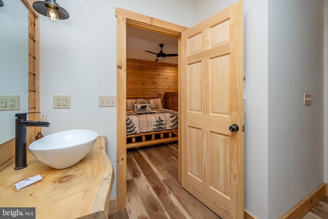 bathroom with hardwood / wood-style floors, ceiling fan, wood walls, and sink