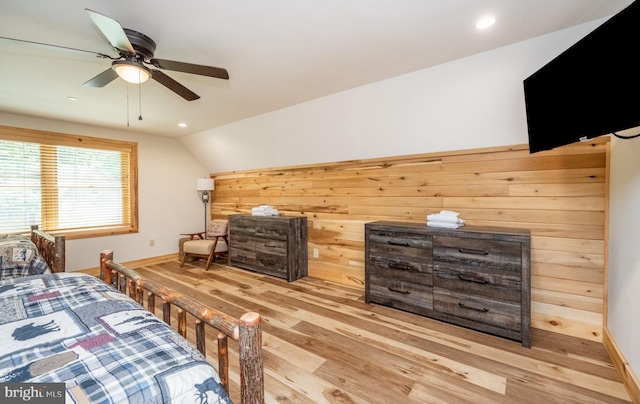 bedroom featuring ceiling fan, light hardwood / wood-style flooring, wooden walls, and vaulted ceiling