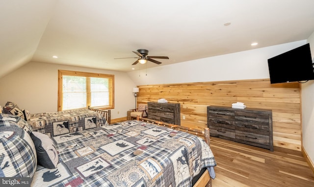 bedroom with ceiling fan, wood walls, light hardwood / wood-style floors, and lofted ceiling