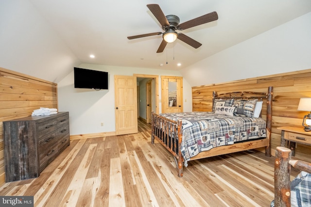 bedroom with light hardwood / wood-style floors, ceiling fan, lofted ceiling, and wood walls