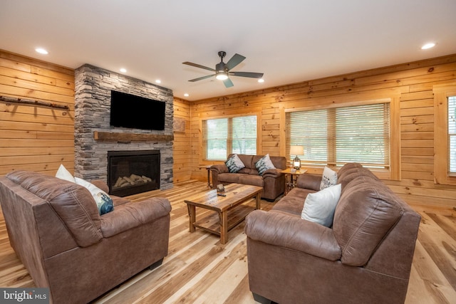 living room featuring ceiling fan, a fireplace, light hardwood / wood-style floors, and wooden walls