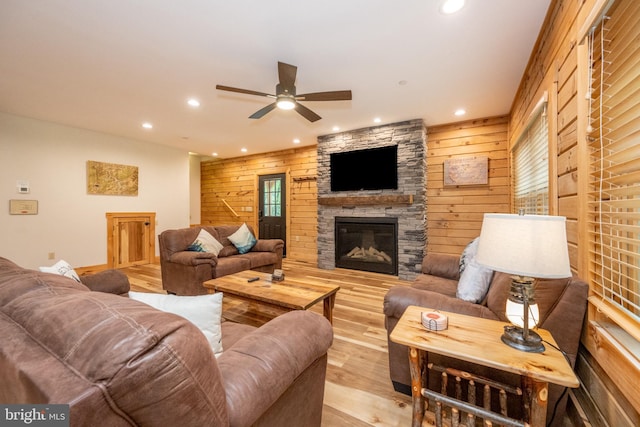 living room featuring light wood-type flooring, a stone fireplace, ceiling fan, and wood walls