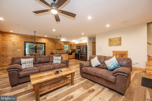 living room with ceiling fan, light wood-type flooring, and wooden walls