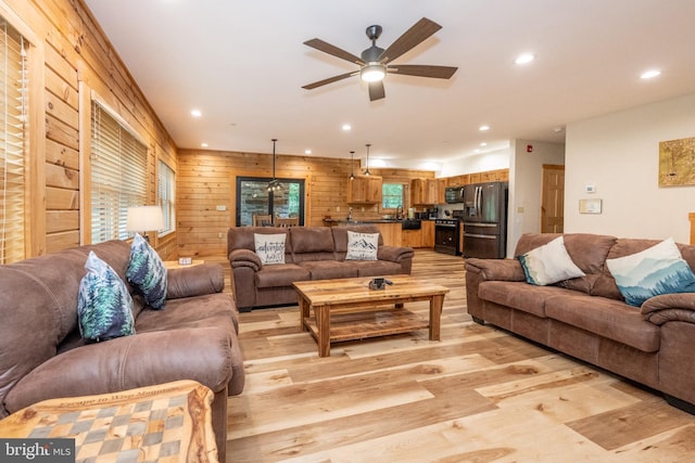 living room featuring ceiling fan, sink, wooden walls, and light hardwood / wood-style flooring