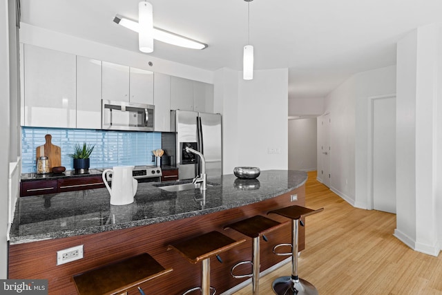 kitchen featuring decorative backsplash, stainless steel appliances, pendant lighting, dark stone countertops, and a breakfast bar area