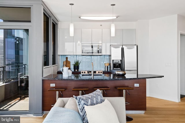 kitchen with white cabinetry, hanging light fixtures, light hardwood / wood-style flooring, a kitchen bar, and appliances with stainless steel finishes