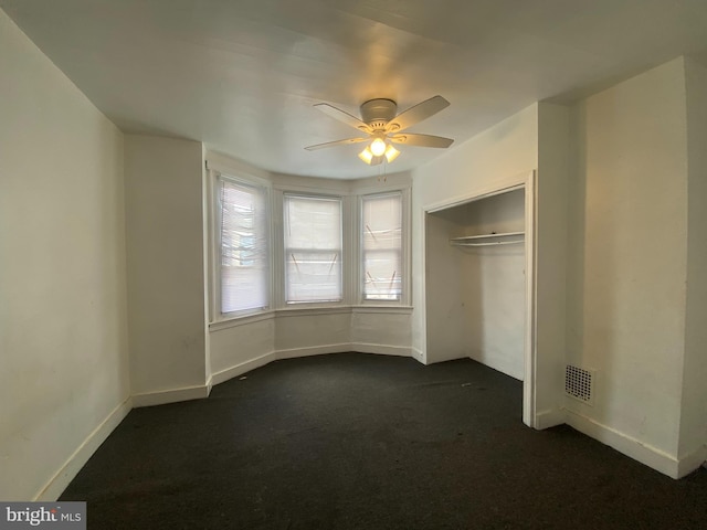 unfurnished bedroom with ceiling fan, a closet, and dark colored carpet